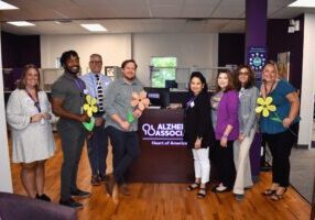 The Alzheimer's Association team stands in front of their logo in their office space, posing for the picture.